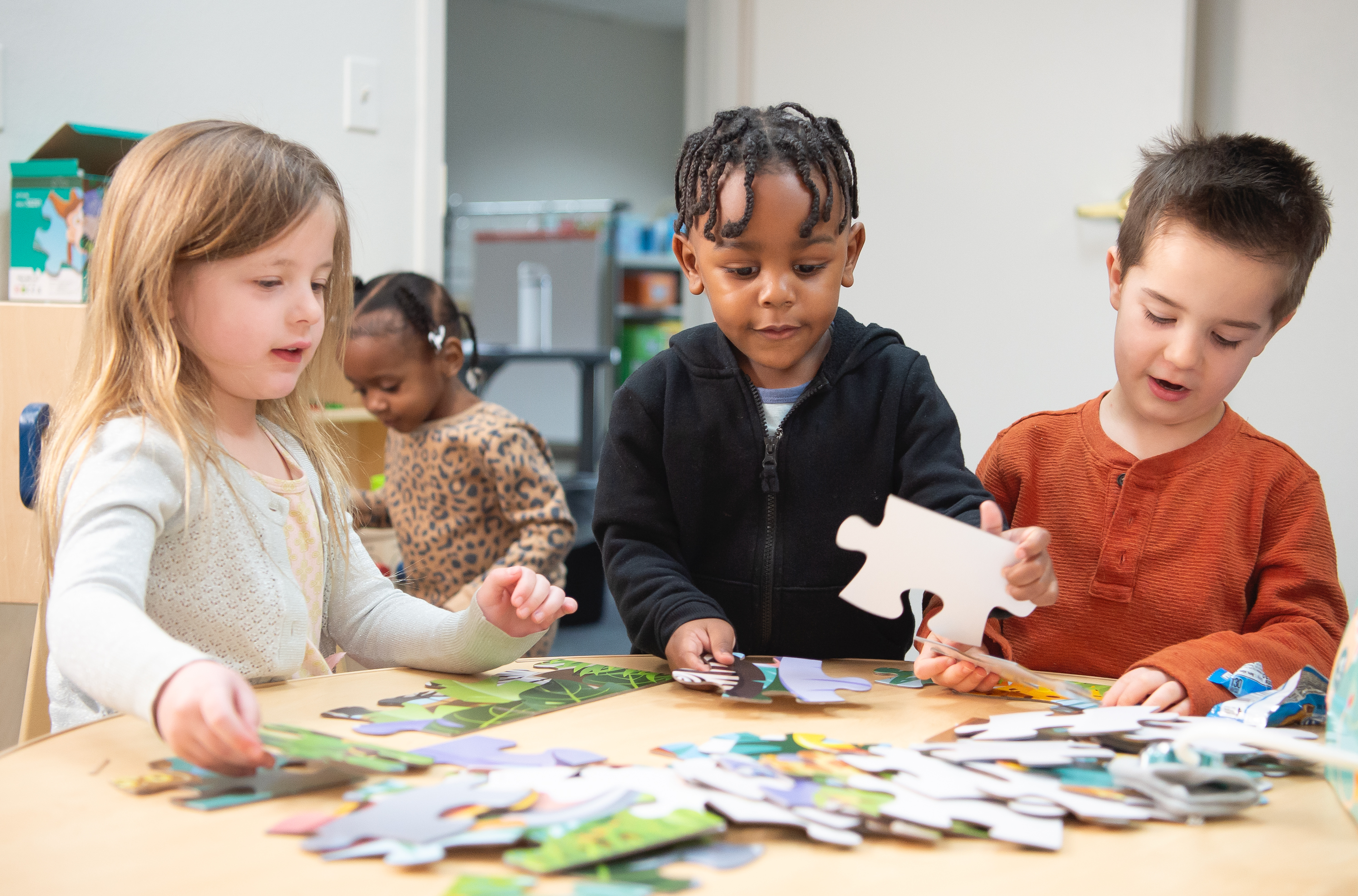 Three toddlers working on a puzzle at a table in a classroom setting. 